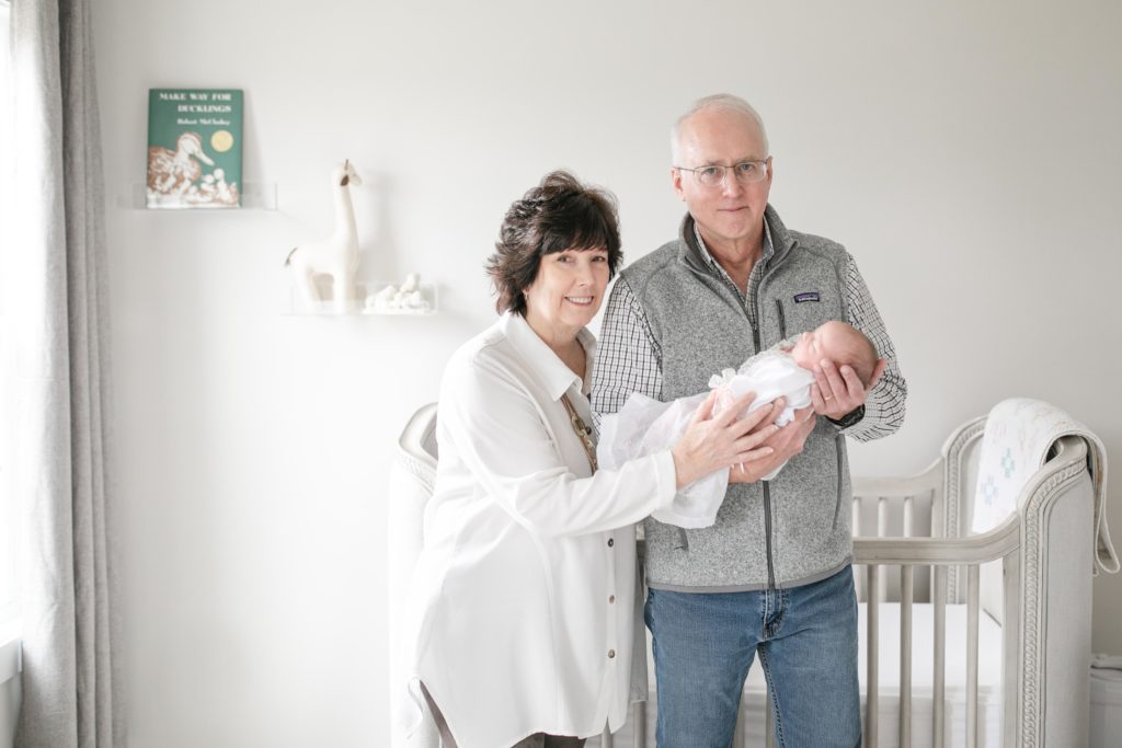 grandparents holding baby Harper in nursery room in front of crib